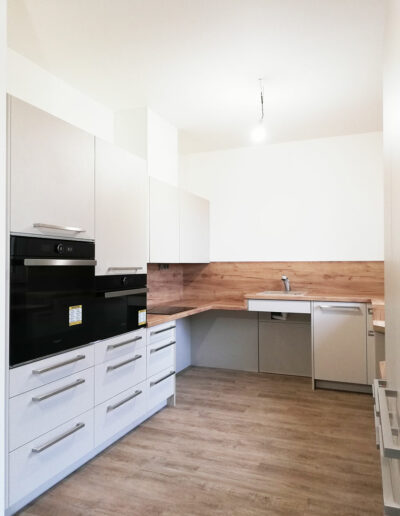 Kuchyň do U pro vozíčkáře v kombinaci bílé barvy a dubu.