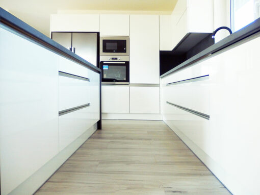 Kuchyň do L s ostrůvkem v bílé lesklé barvě.