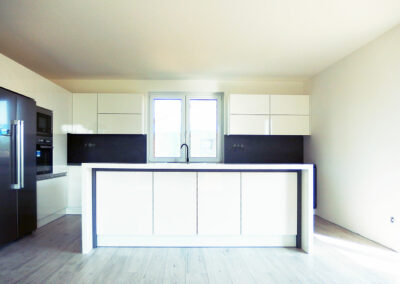 Kuchyň do L s ostrůvkem v bílém lesku a tmavé pracovní desce.