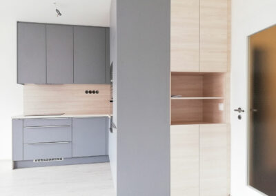 Kuchyň do L s dvířky v světlé šedé barvě a pracovní deskou ve světlém dřevě.