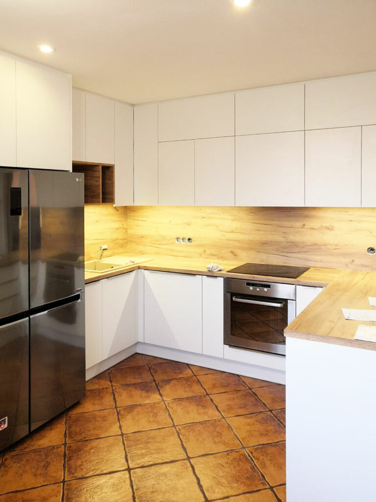 Kuchyň do U v kombinaci bílých dvířek a dřevěné pracovní desky a zástěny.