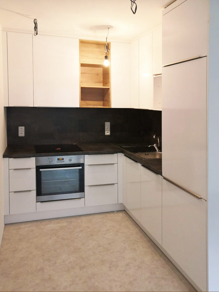 Kuchyň do L s býlým lesklými dvířky a otevřenou dřevěnou částí.