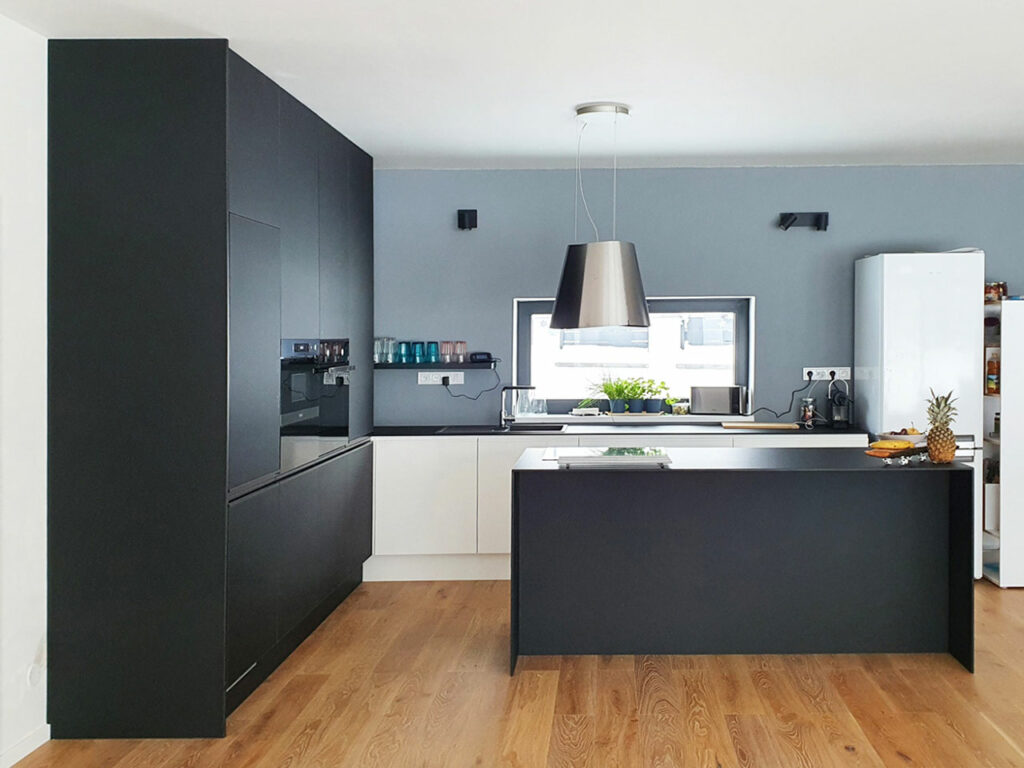 Krásná kuchyň v kombinaci bílého lesku a černého matu. Vše završeno tenkou pracovní deskou z kompaktního laminátu a úchytkami lakovanými v barvách kuchyně.