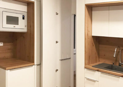 Kuchyň  do L v oblíbené kombinaci bílé a přírodního dubového dřeva. Část kuchyně funguje jako prostup do ložnice.