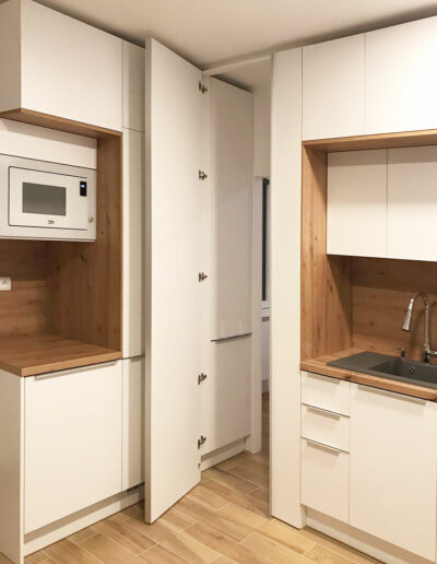 Kuchyň  do L v oblíbené kombinaci bílé a přírodního dubového dřeva. Část kuchyně funguje jako prostup do ložnice.