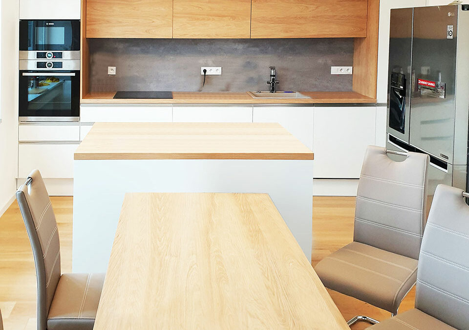 Rovná kuchyň s ostrůvkem jídelním stolem v kombinaci bílé lesklé a dubu.