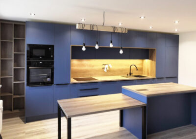 Rovná kuchyň v modré barvě s dřevěnou pracovní deskou a zástěnou.