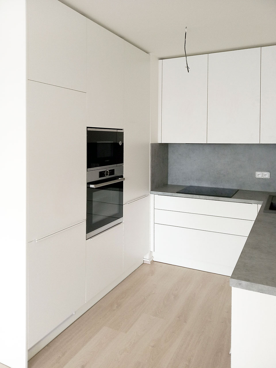Bílá kuchyň do U s pracovní deskou a zástěnou v dekoru světlý beton.