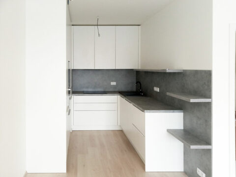 Bílá kuchyň do U s pracovní deskou, zástěnou a poličkami v dekoru světlý beton.