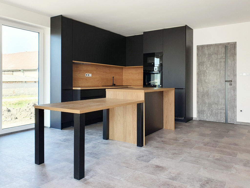 Kuchyň do L s ostrůvkem a jídelním stolem v kombinaci černé matné a přírodního dubu.