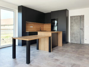 Kuchyň do L s ostrůvkem a jídelním stolem v kombinaci černé matné a přírodního dubu.