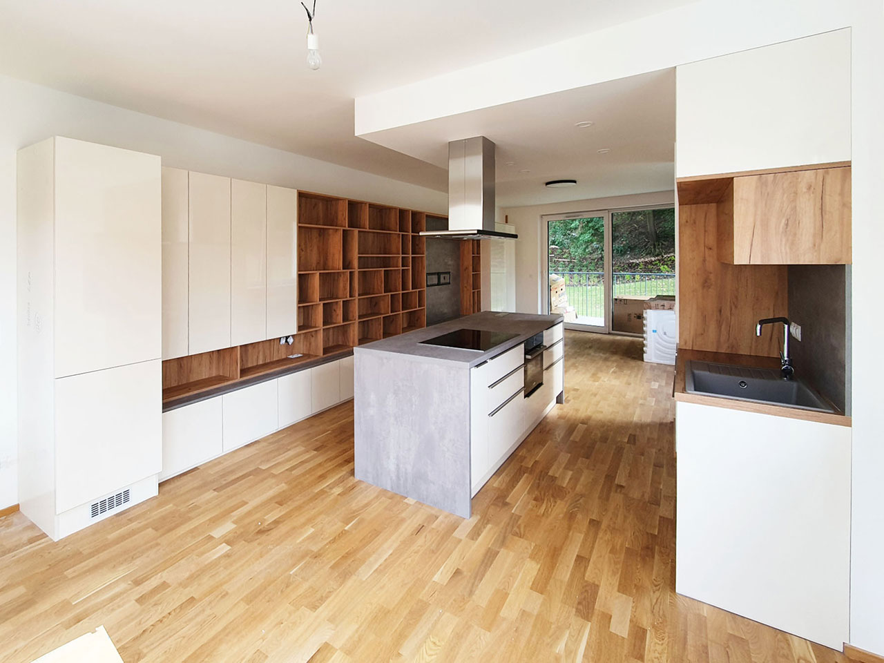 Kuchyň s ostrůvkem a obývací stěnou v kombinaci krémové lesklé barvy a přírodní dub.