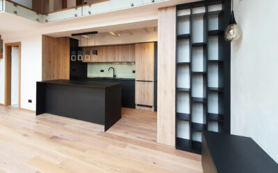 Kuchyň do podkroví s otevřenou knihovnou s černou pracovní deskou z kompaktního laminátu.